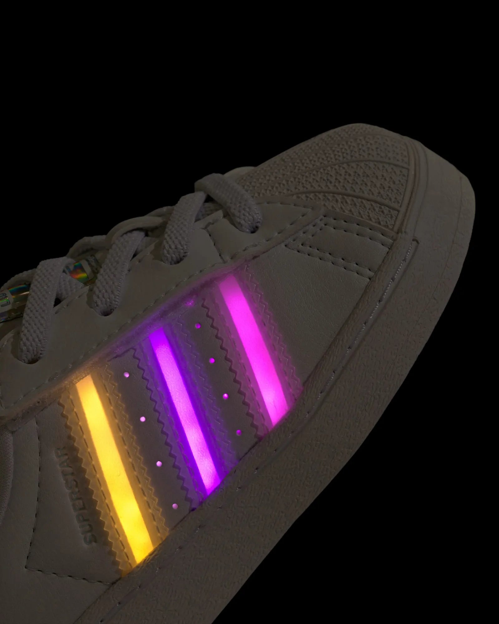 White sneaker with glowing yellow and purple stripes on a black background